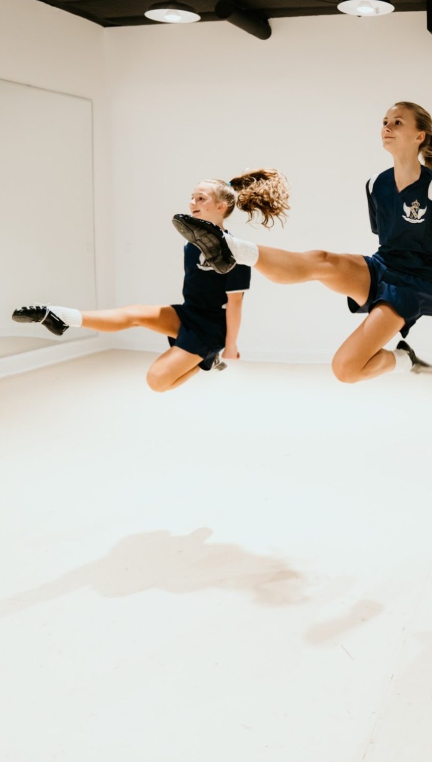 Two students leaping in unison with their right legs straight out in front of them
